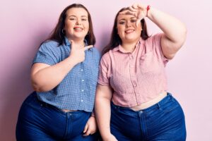 Young plus size twins wearing casual clothes smiling making frame with hands and fingers with happy face. creativity and photography concept.
